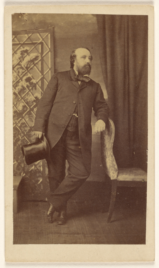 Full Bearded Man Holding A Top Hat Standing Leaning On Chair