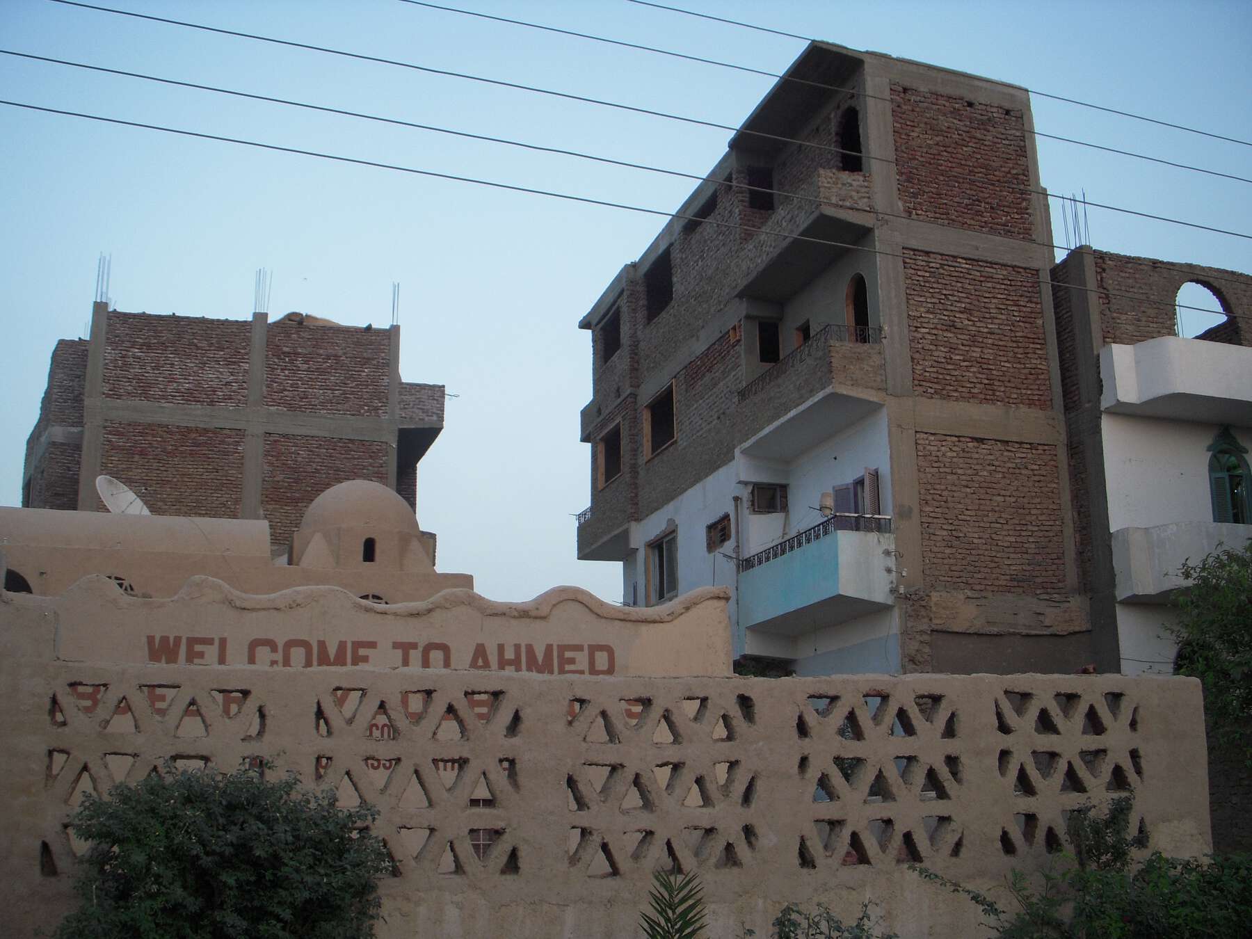 Concrete fence with triangular holes, behind it are both older single-story and newer multistory buildings.