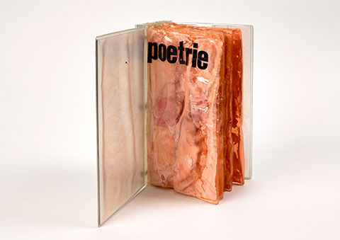 A book with a Plexiglas exterior stands upright with the cover open to reveal distressed pages of plastic-sealed cheese. The title poetrie appears in lowercase letters across the top of the first page. 