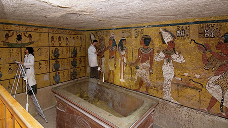 Two people in white lab coats work in a room with Egyptian art on the walls.