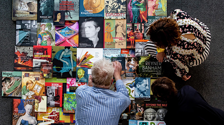 View from above of three people standing over an array of brightly colored books.