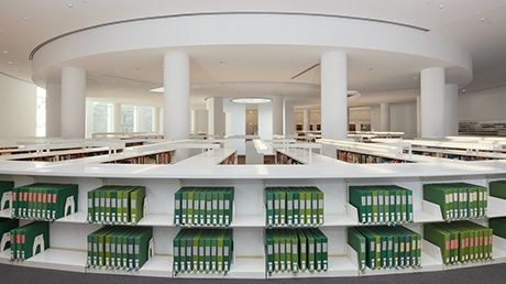 A white room with white bookshelves holding green binders. 