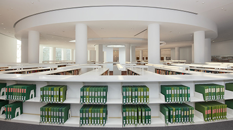 A white room with white bookshelves holding green binders.