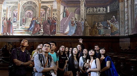 Groups of people looking up at a large wall fresco of people wearing togas.