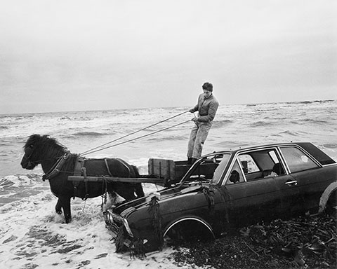 A Car Dumped on the Beach Has to Be Outmanoeuvred by the Seacoalers, Lynemouth, Northumberland, 1982, Chris Killip, gelatin silver print. Courtesy of and © Chris Killip.