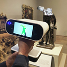 Hands holding up a digital scanner to a small bronze statue of a man