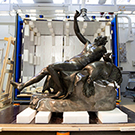 A bronze statue of a reclining satyr in a large conservation studio