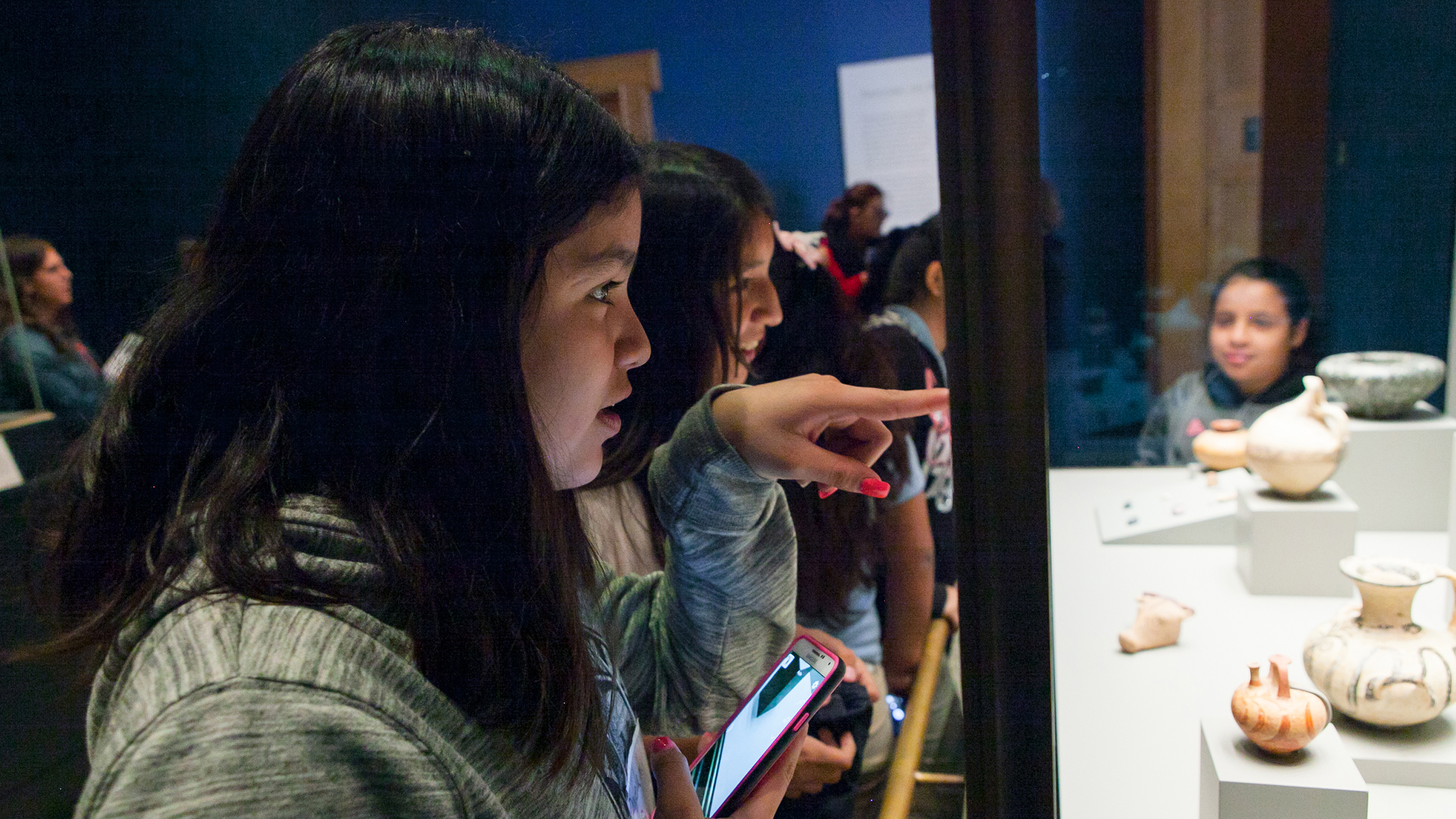  A young girl points at small ceramic pots behind display glass