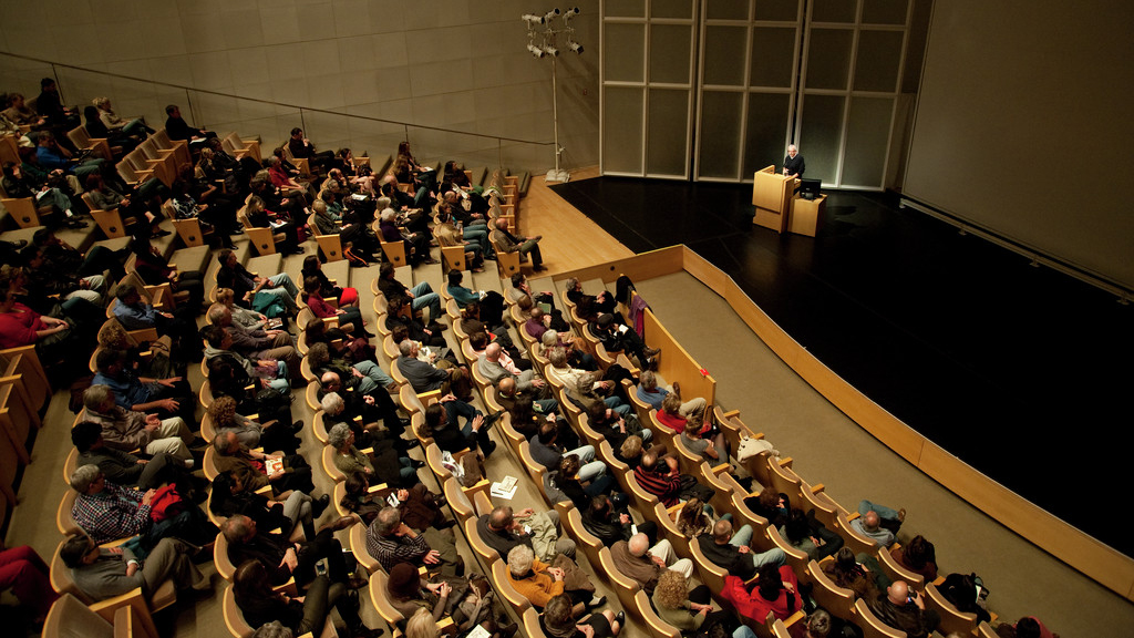 a large audience sits in an auditorium in front of someone at a podium