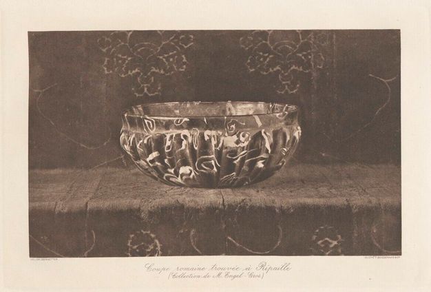 A deep, round glass bowl with vertical channels rests on a patterned surface with floral designs. The bowl is translucent with swirling, irregular internal patterns.