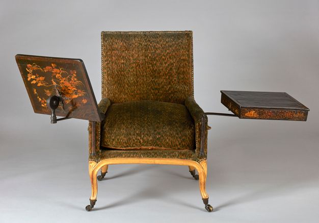 Cushioned and wheeled armchair featuring a wooden tilting stand on the right and a desk on the left. Both the stand and the desk exhibit a lacquered design showcasing botanical motifs.