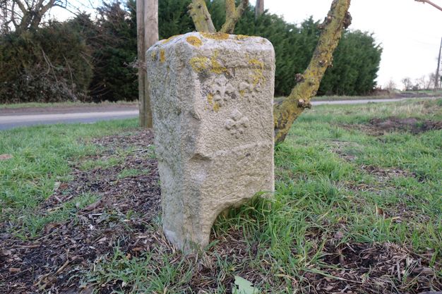 Rectangular stone monolith featuring three fleur-de-lis motifs in low relief on its upper half.