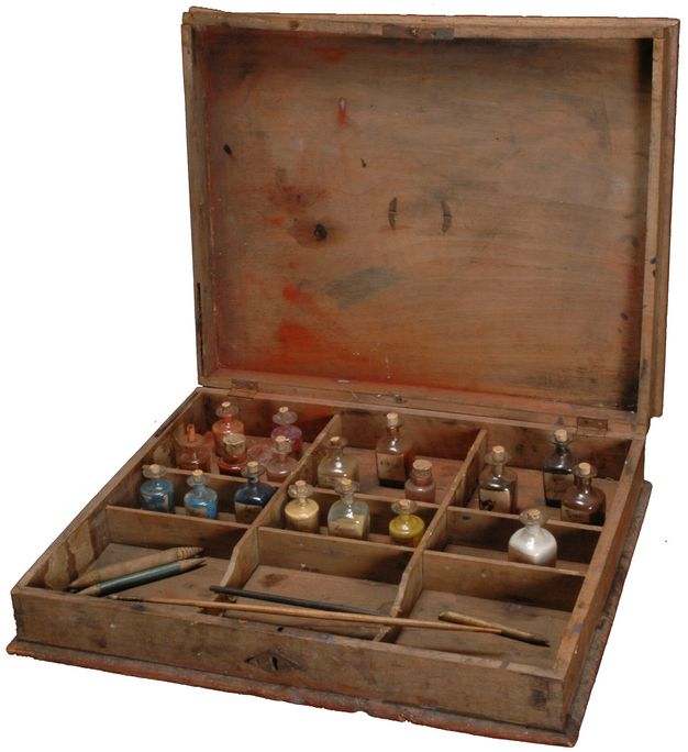 Shallow wooden box divided into nine compartments holding miniature glass bottles that contain ground pigments as well as fine brushes and other tools.