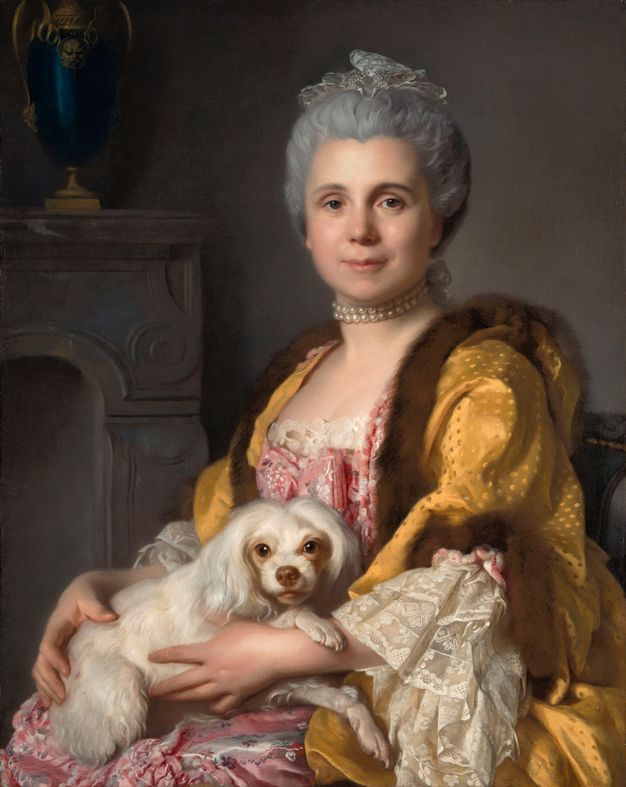 Portrait of a lavishly dressed woman holding a white, spaniel dog on her lap. The woman uses her hands to hold the animal close to her. She is shown wearing a lace hair ornament, a pearl necklace, a pink dress with ruffles at the chest and the sleeves, and a yellow coat.