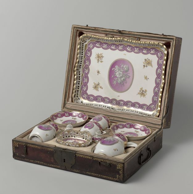 Open wooden box containing a porcelain coffee service with floral decoration in pink and gold. The service includes a tray, two cups with their saucers, a coffee pot, a sugar bowl, and a creamer.