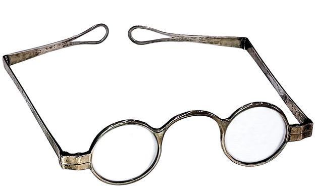 Glasses of the kind worn by the individual in figure 65. They feature a metal frame, rounded glass lenses, and double-hinged arms that wrap around the head of their user.