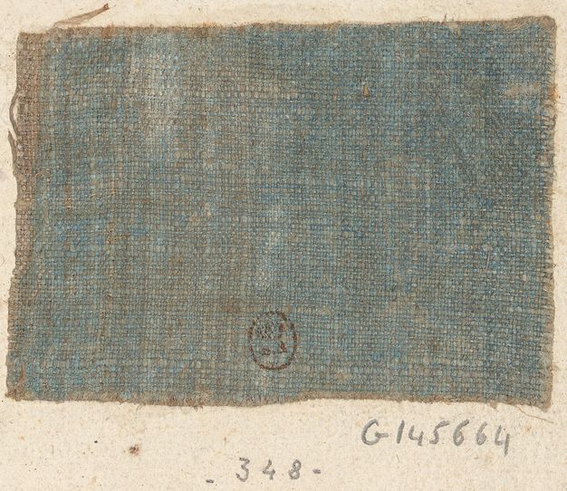 Square piece of blue fabric attached to a page. The fabric shows a small circular stamp along its bottom edge. Below the fabric, there are numerical annotations written in pencil.