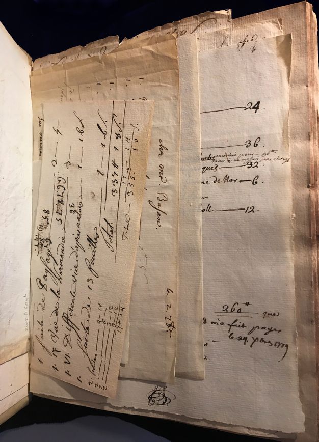 Loose stacks of paper tucked inside a bound notebook. The pages show slight damage on the edges and feature text handwritten in ink.