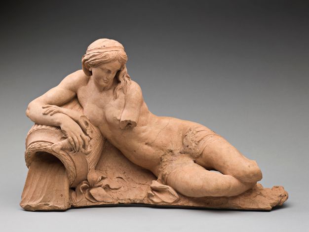 Terracotta sculpture depicting a nude woman reclining over a vase from which water emerges. The middle section of the figure’s left arm is broken as may be the case of her lower legs which cannot be clearly seen in the photograph.