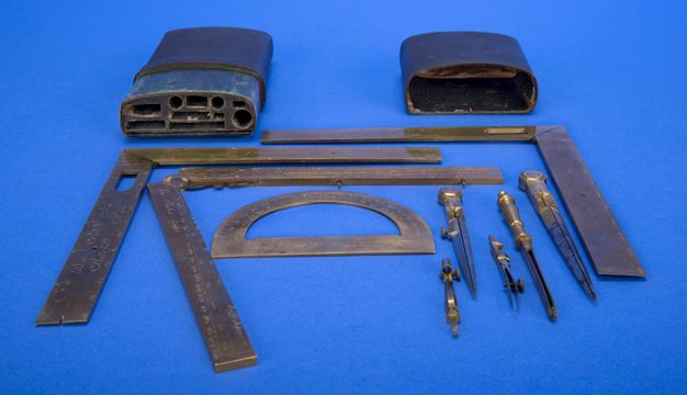 Photograph of a case and drawing instruments, including a protractor and folding rulers, against a blue background. The case has compartments in which the tools can be inserted.