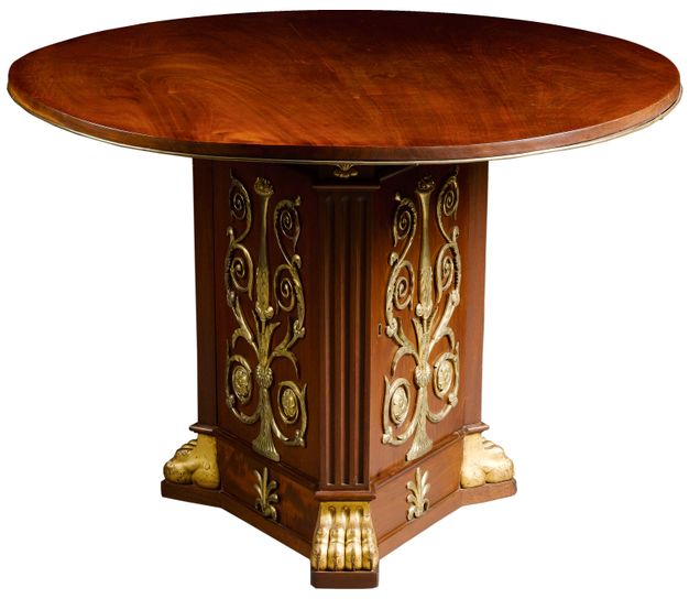 Wooden table with a circular top and a triform pedestal base with fluted cantered corners. The base and feet exhibit gilt-bronze ornamentation. It resembles that shown in Figure 163.