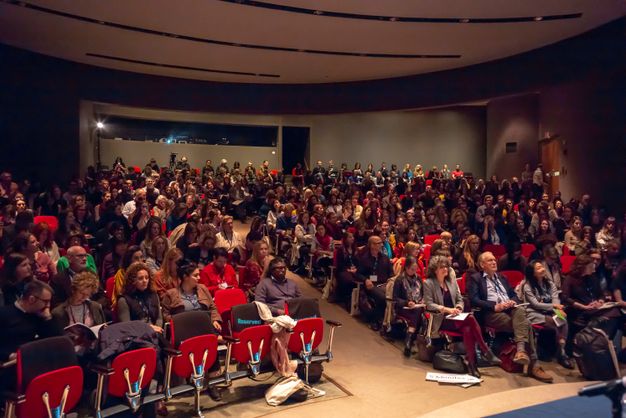 An auditorium filled with attendees watch a presentation.