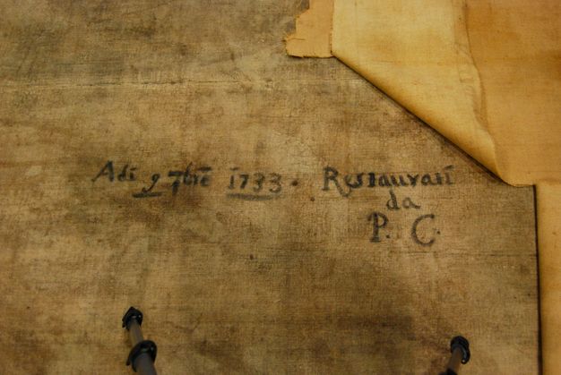 Photograph of a yellowed painting lining that is being removed, revealing an artistic signature.