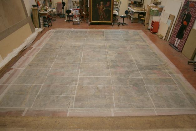 Wide photograph of the same painting, still laid flat on the floor but with treatment paper atop it.