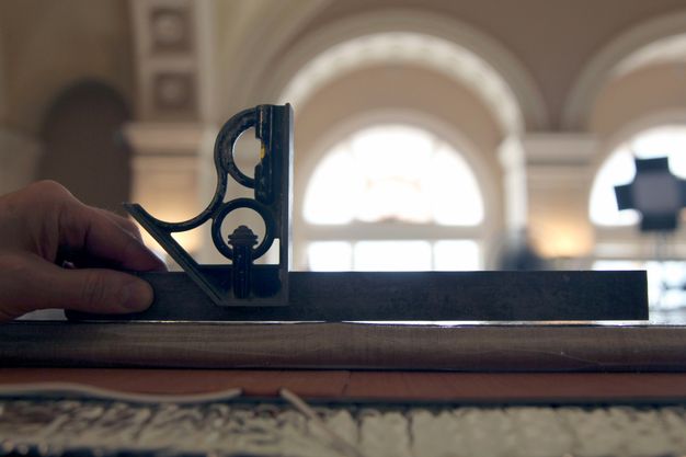 Close up photo of a hand (left) using a tool to examine the seams of the painting panel.