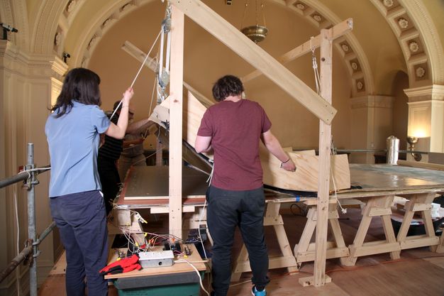 Photo of three people rigging the wooden panel in 12.6 to a table.