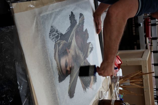 Photo of a conservator as they treat the same portrait. A white tissue is placed over the painting as the conservator brushes over it with resin.