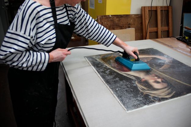 Photo of a conservator in a striped shirt ironing a painting during treatment.