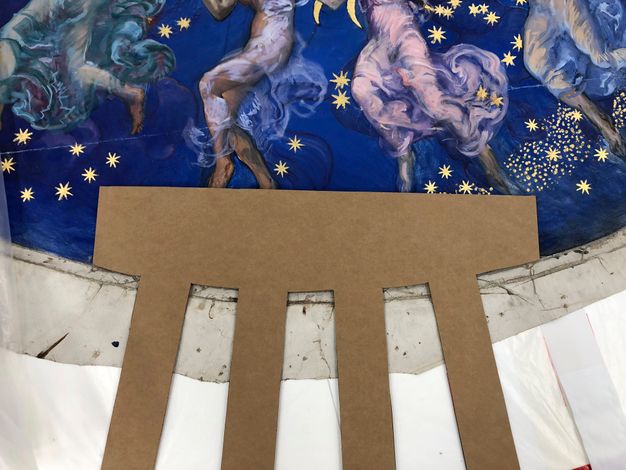 Close up photo of a piece of cardboard being used to outline strips for the painting (24.1) canvas.