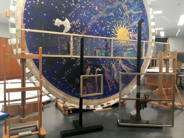 Wide photo of the painting (24.1) held up in a frame and platform in the lab.