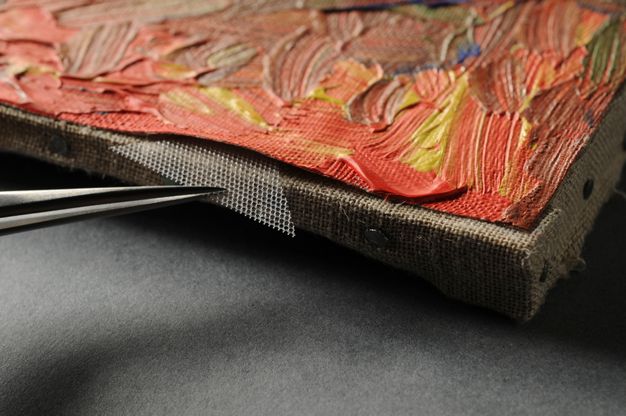 Tweezers slide a small piece of honeycomb-patterned mesh between the original and lining canvas.