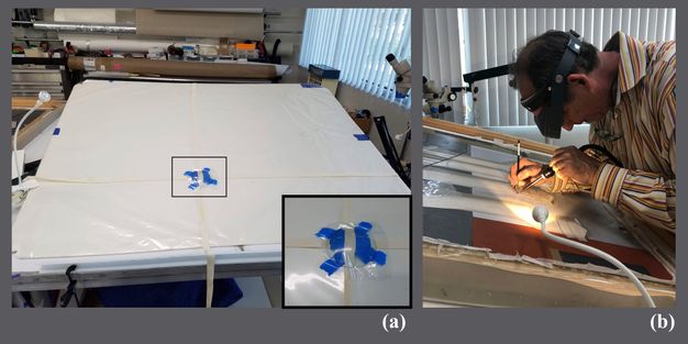 Image A shows a large piece of board laid out on a table with two lengths of tape adhered to it vertically and horizontally. Underneath the point where the strips of tape intersect is a piece of glass with Mylar placed over it; there is also a detail of this intersection. Image B shows a man with a headlamp hunched over a painting that is placed on the surface of the board with the attached glass from image A. He carefully works on the painting using a device that supplies hot air in one hand and a silicone shaper in his other.
