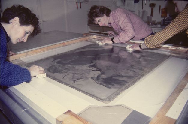Photograph of three people leaning over a table whilst fixing a painting lining.