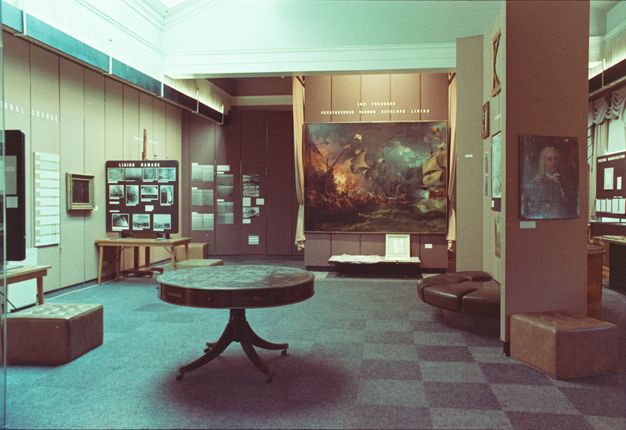 Photo of the interior of a conservation studio. Paintings and photographs scatter the walls, with a table at the center of the room.