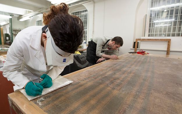 Photograph of two painting conservators leadning over a table and examining the back of a painting.