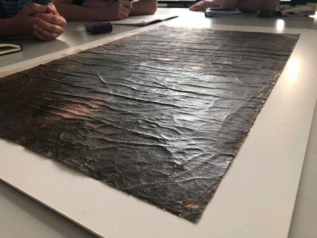 Photograph close-up of a portrait painting prior to treatment, which has an aged, wrinkling canvas surface.