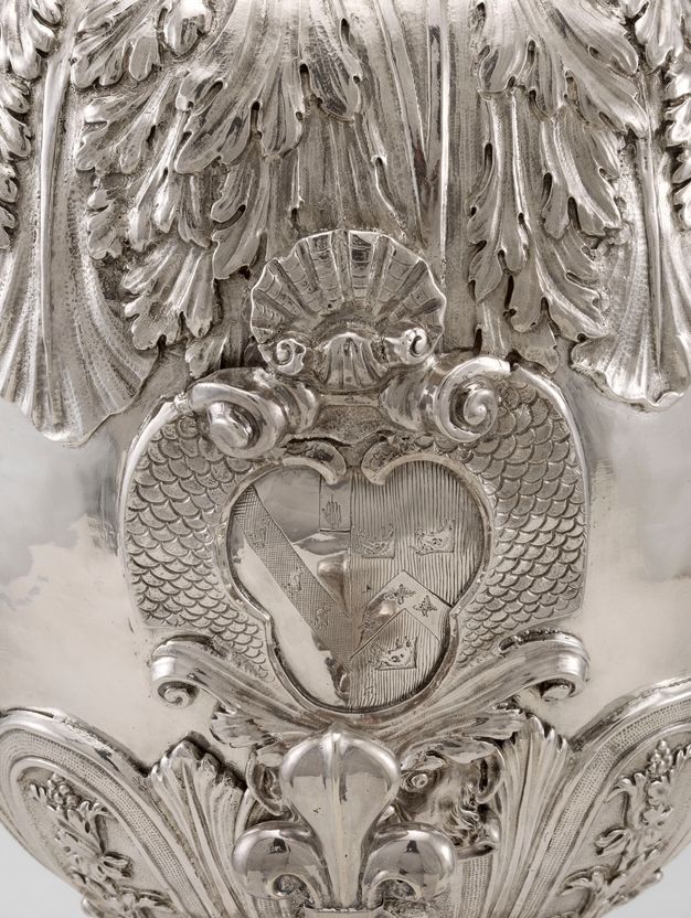 A family insignia framed by scales and surrounded by leafy decorations at the center of a silver vessel.