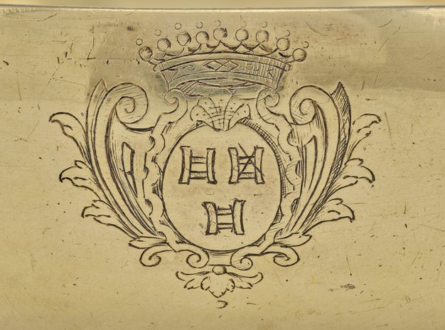 Close-up of a coat of arms with three H shapes framed by flourishes and leaves, topped with a shell and crown.