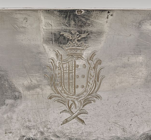 Close-up of a coat of arms with a center design of two ladders and two rows of three dots framed by branches and topped with a crown and eagle.