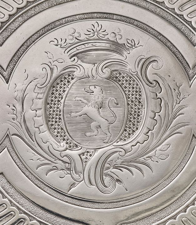 Close-up of a coat of arms featuring a roaring lion framed by palm fronts and topped by a crown.