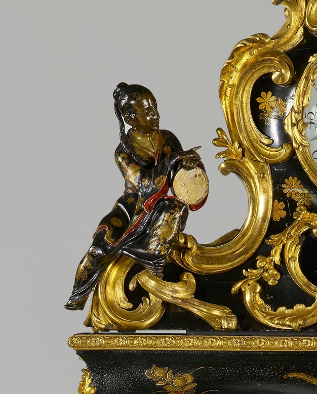 Close-up of a figure with a ponytail wearing a black robe with gold and red accents lounging next to a clock.