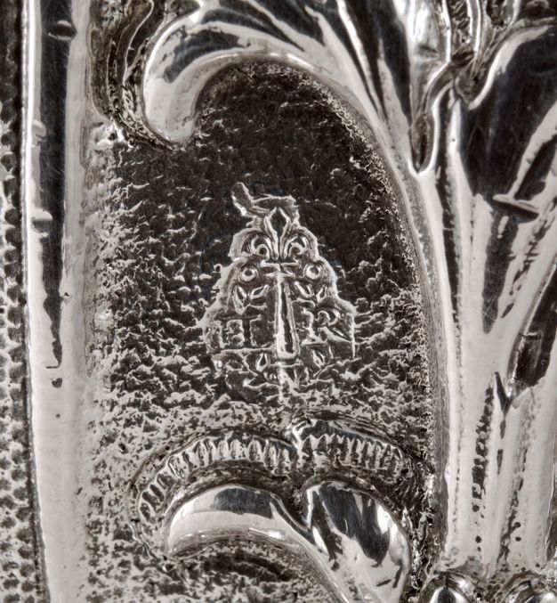 Close-up of the letters IR surrounding a bar topped with a stylized lily stamped on a water fountain.
