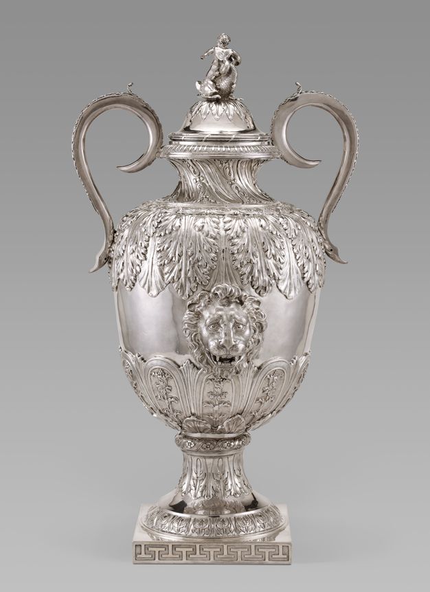 Backside of a silver vessel decorated with leaves, a lion head, and a boy holding a conch shell.