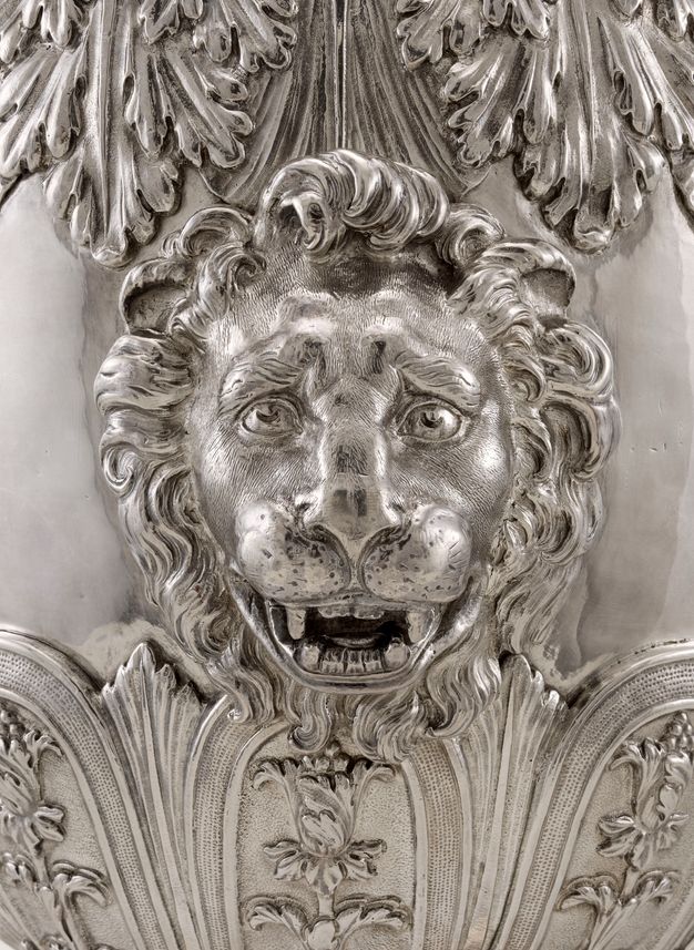 A lion's face surrounded by leaves and flowers on a silver vessel.