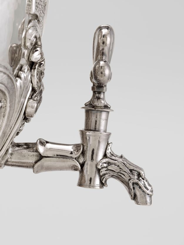 Silver spout protruding from a bird's mouth with a large handle.