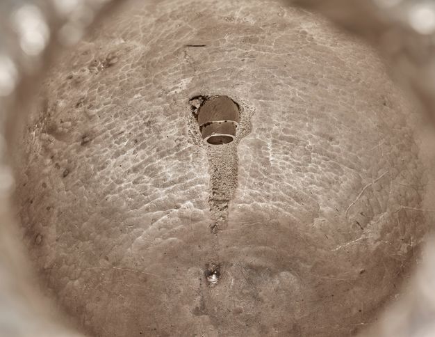 Textured interior of a silver vessel revealing the base of a spigot.